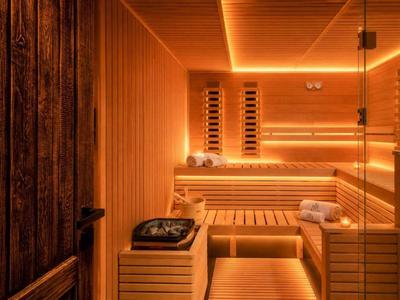 Moderner Sauna-Raum mit Holzbänken und warmem, orangefarbenem Licht.