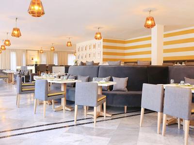 Nowoczesna restauracja hotelowa z szarymi krzesłami, drewnianymi ramami i ciepłym oświetleniem.