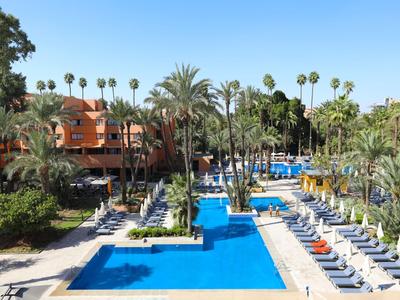 Hotel z dwoma niebieskimi basenami otoczonymi palmami i leżakami pod czystym niebem.