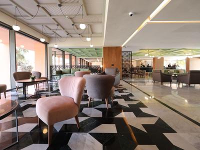 Nowoczesna przestrzeń wypoczynkowa hotelu z różowymi fotelami i geometrycznym wzorem podłogi.