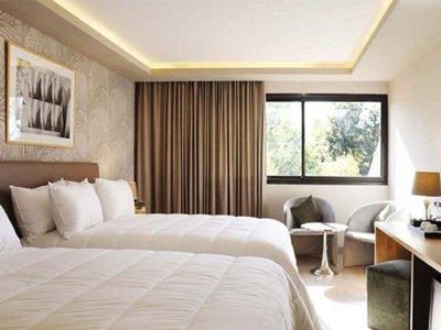 Nowoczesny pokój hotelowy z dwoma łóżkami podwójnymi, sofą i dużym oknem.