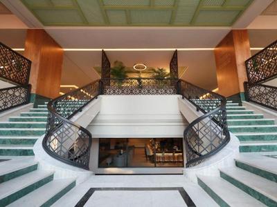 Luksusowy hol hotelowy z symetrycznymi schodami, zielonym dywanem i eleganckimi balustradami.