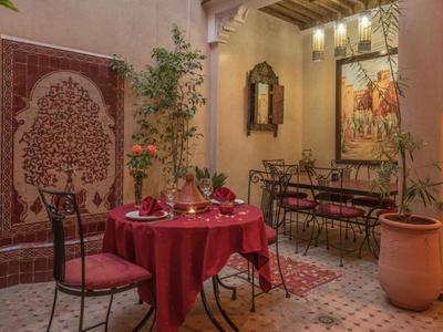 Innenhof mit kunstvoll verziertem Wandmosaik, rot gedecktem Tisch und Stühlen in warmem Licht.