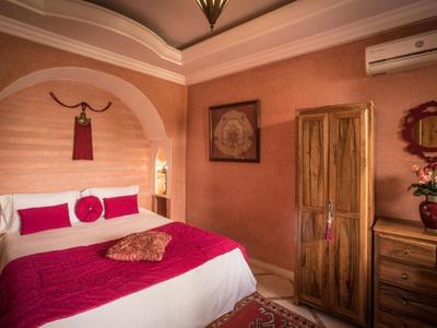 Gemütliches Hotelzimmer mit roter Bettdecke, Holzmöbeln und dekorativem Wandhänger.