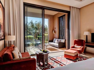 Hotel room with sofa, armchair, balcony furniture, and view of greenery.