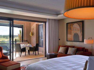 Bright hotel room with bed, sofa, balcony area, and countryside view in daylight.