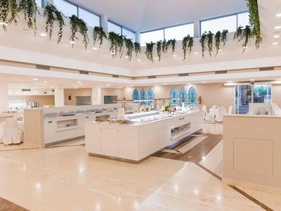 Heller, moderner Speisesaal mit weißen Möbeln und hängenden Pflanzen unter Oberlichtern.