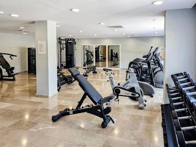 Moderner Fitnessraum mit Trainingsbank, Laufbändern, Hanteln und Kraftgeräten im Hotel.