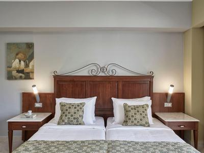 Zwei Einzelbetten mit Holzkopfteil, weißen Bettdecken und dekorativen Kissen in einem Hotelzimmer.