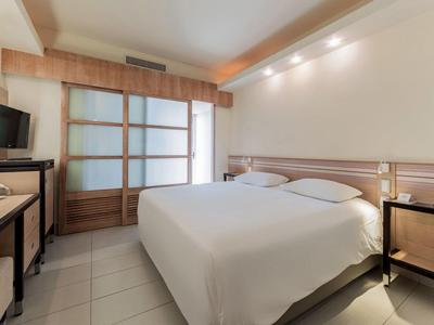 Helles Hotelzimmer mit großem Doppelbett, Schreibtisch und Fernseher, neutrale Farben.