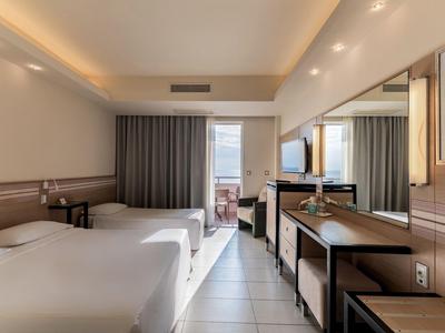Moderner Hotelraum mit zwei Einzelbetten, Schreibtisch, TV und Balkon mit Meerblick.