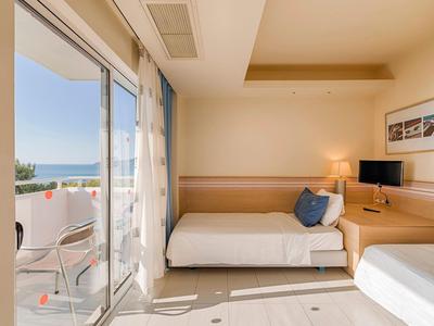 Helles Hotelzimmer mit Doppelbett, Balkonblick aufs Meer und moderner Einrichtung.