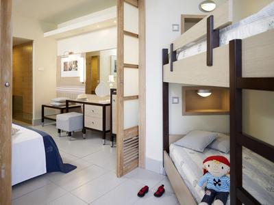 Hotelzimmer mit Etagenbett, Einzelbett, Schreibtisch und hellen Wänden.