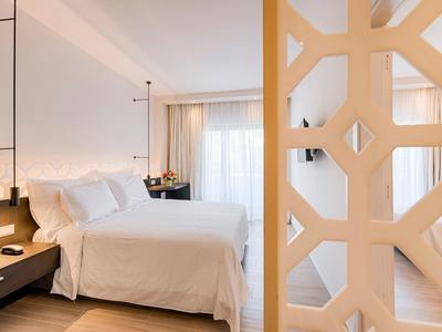 Helles Hotelzimmer mit großem Bett, weißer Bettwäsche und modernem Trennwand-Design.