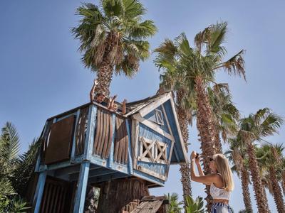Ein Baumhaus im tropischen Stil zwischen Palmen unter blauem Himmel.