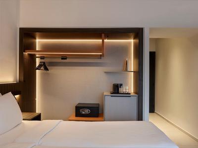 Moderner Hotelzimmerbereich mit begehbarem Kleiderschrank, Safe und Minibar unter warmem Licht.