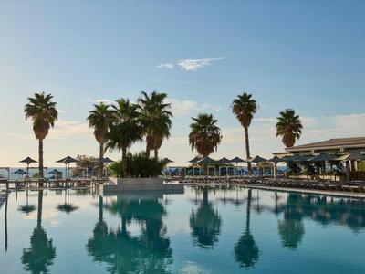 Großer Pool mit Palmen und Sonnenschirmen in einem Hotelresort bei klarem Himmel.