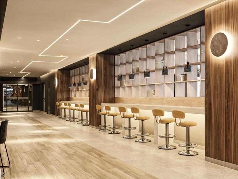 Moderner Hotelbarbereich mit Lederhockern entlang einer langen Bar und holzvertäfelten Wänden.