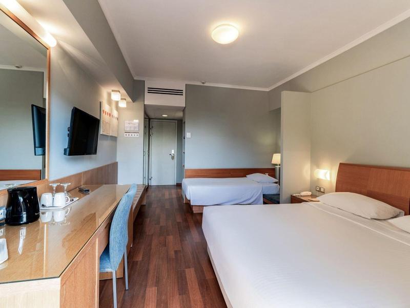 Modernes Hotelzimmer mit Doppelbett, Einzelbett, Schreibtisch und Holzfußboden, Beleuchtung an der Wand.