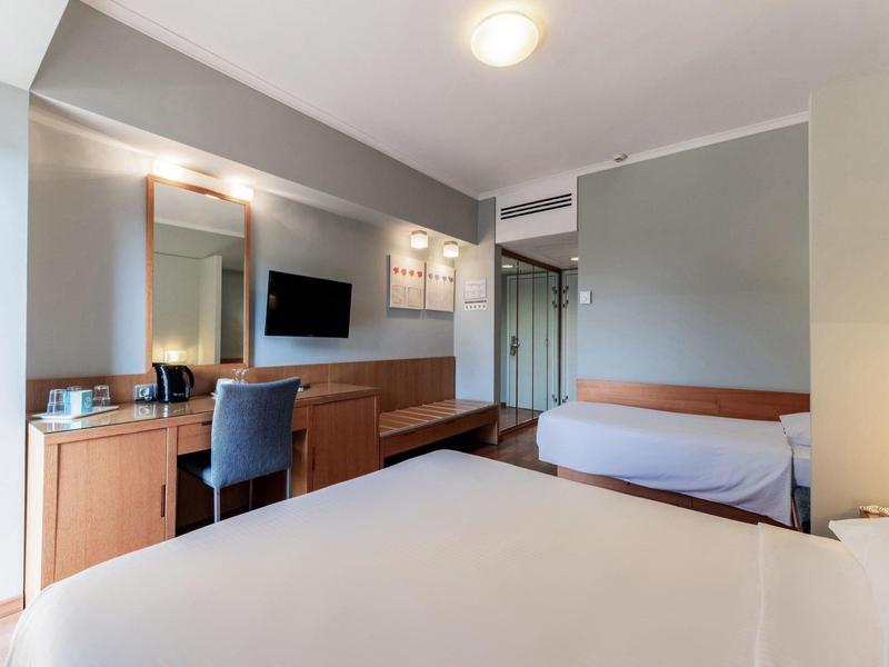 Modern eingerichtetes Hotelzimmer mit Doppelbett, Schreibtisch, Fernseher und kleinem Sofa.