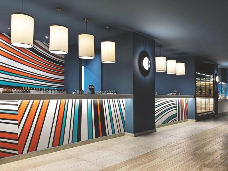 Moderner Hotel-Empfang mit farbenfrohem gestreiftem Tresen und Hängeleuchten.