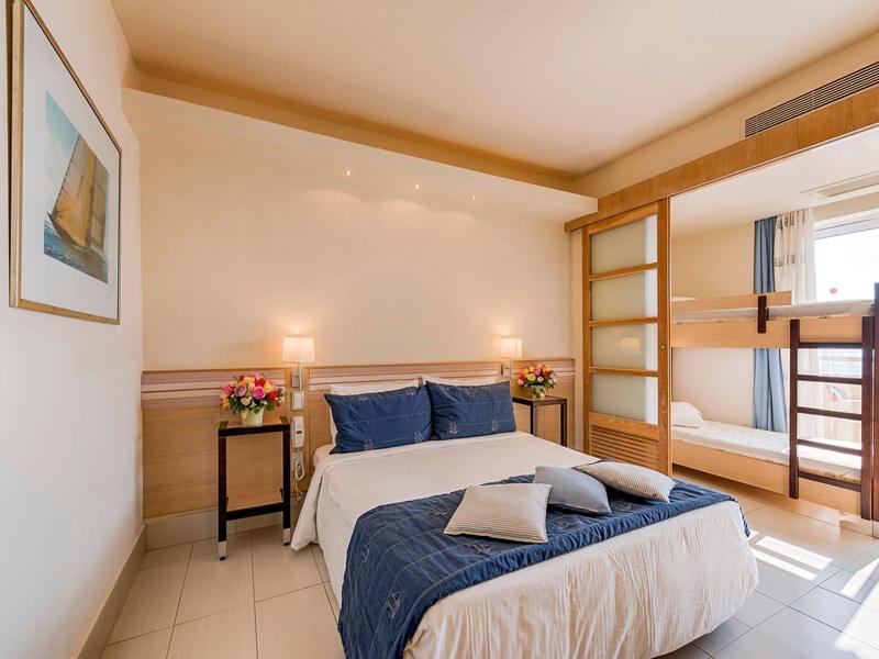 Helles Hotelzimmer mit Doppelbett, Etagenbett und moderner Einrichtung.