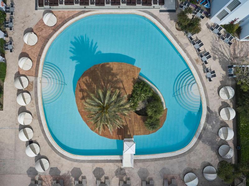 Luftaufnahme eines runden Pools mit Sonnenschirmen und Liegestühlen.