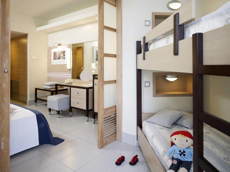 Hell eingerichtetes Hotelzimmer mit Doppelbett und Etagenbett, moderner Einrichtung und kindgerechtem Spielzeug.