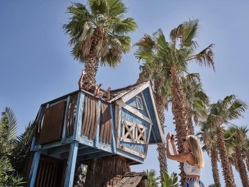 Ein Baumhaus im tropischen Stil zwischen Palmen unter blauem Himmel.