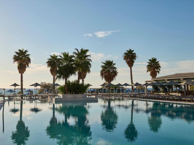 Ruhepool mit Sonnenliegen, Palmen und klarem Himmel in einem Hotelresort.