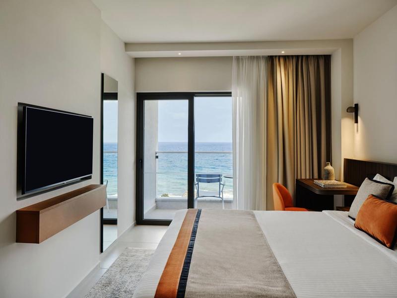 Modernes Hotelzimmer mit Meerblick, großem Bett, TV und Schreibtisch an der Seite.