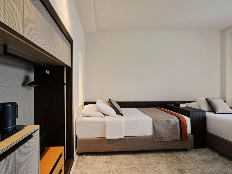 Modern eingerichtetes Hotelzimmer mit zwei Betten, neutralen Farben und minimalistischem Design.