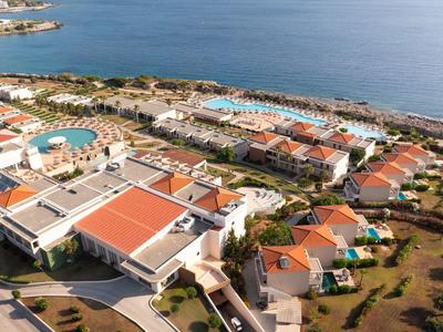 Resort mit roten Dächern, Pools und Gärten an der Küste mit blauem Meer im Hintergrund.