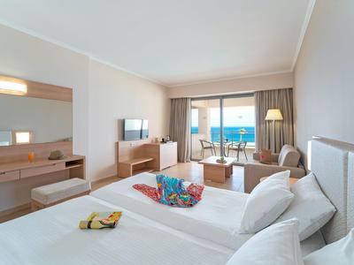 Modernes Hotelzimmer mit Doppelbett, Fernseher, Sitzbereich und Meerblick durch große Fenster.