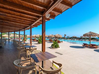 Überdachte Terrasse mit Holztischen und Stühlen neben einem Pool mit Liegestühlen und Sonnenschirmen.