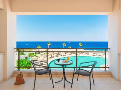 Balkon mit Tisch, zwei Stühlen, mit Blick auf Strand, Meer und blauem Himmel im Hintergrund.