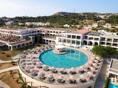 Großes Hotel mit rundem Außenpool, vielen Sonnenliegen und umliegenden Gebäuden in Hügelumgebung.