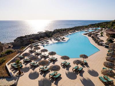 Großer Pool mit Sonnenschirmen und Liegestühlen neben dem Meer bei Sonnenuntergang.
