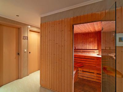 Flur mit Holztür links und Zutritt zu einer Sauna mit rot beleuteten Holzbänken rechts.