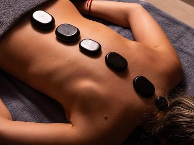 Person liegt bäuchlings mit schwarzen heißen Steinen auf dem Rücken zur Massage bereit.