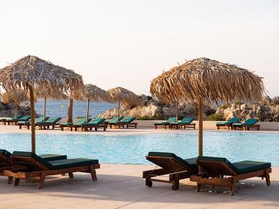 Sonnenliegen und Strohdach-Sonnenschirme am Pool mit Blick auf das Meer.