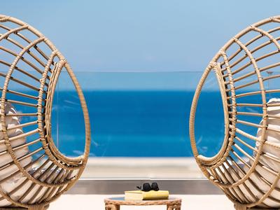 Zwei runde Korbstühle mit Blick auf das blaue Meer und den Himmel am Hotelbalkon.