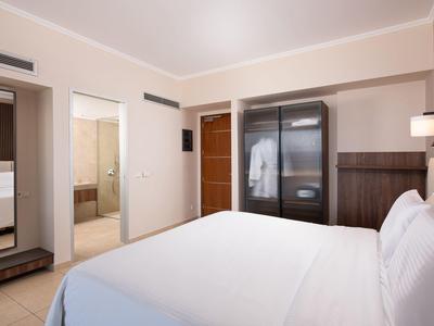 Helles Hotelzimmer mit Doppelbett, offenem Schrank und angrenzendem Bad.