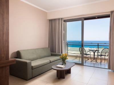 Modernes Hotelzimmer mit Sofa, Tisch und Balkon mit Meerblick und Sitzgelegenheit.