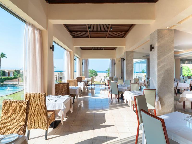 Offenes, helles Restaurant mit Blick auf Pool und Garten, dekoriert mit Holzmöbeln und weißen Tischen.