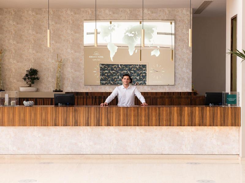 Eleganter Hotelempfang mit dunklem Holz, heller Wand und freundlichem Mitarbeiter hinter Tresen.