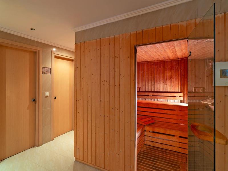 Flur mit Holztür links und Zutritt zu einer Sauna mit rot beleuteten Holzbänken rechts.