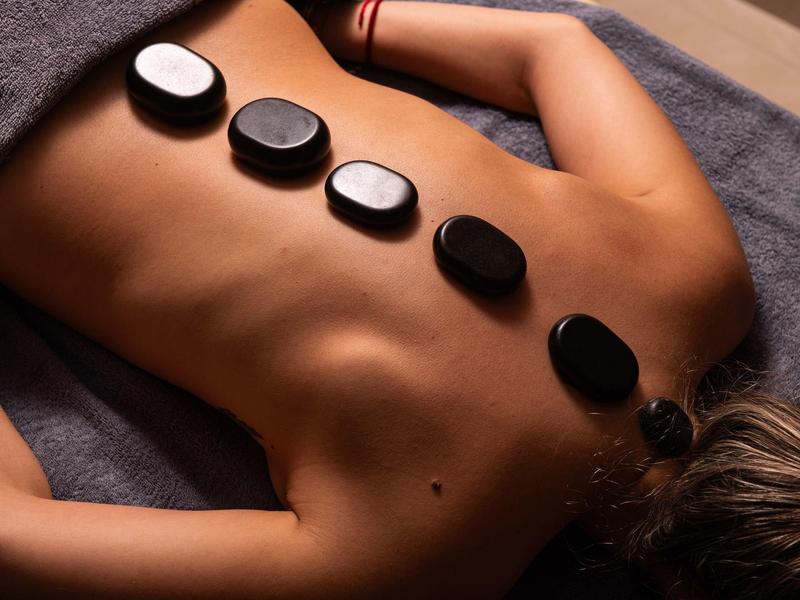 Person liegt bäuchlings mit schwarzen heißen Steinen auf dem Rücken zur Massage bereit.
