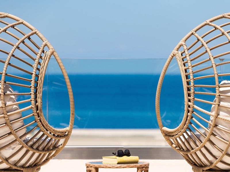 Zwei runde Stühle und ein kleiner Tisch mit Meerblick an einem sonnigen Tag.