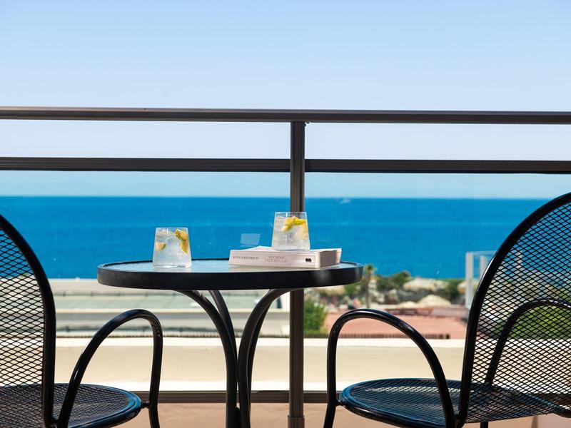 Balkon mit Tisch und zwei Stühlen mit Blick auf das blaue Meer und klaren Himmel.
